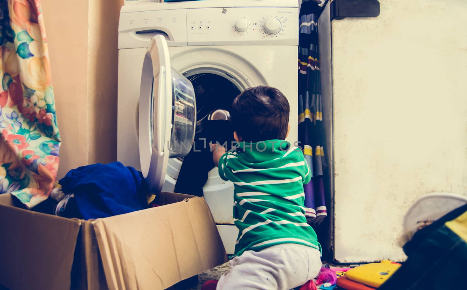 One and the half years old baby boy helping his mom by putting clothes in washing machine