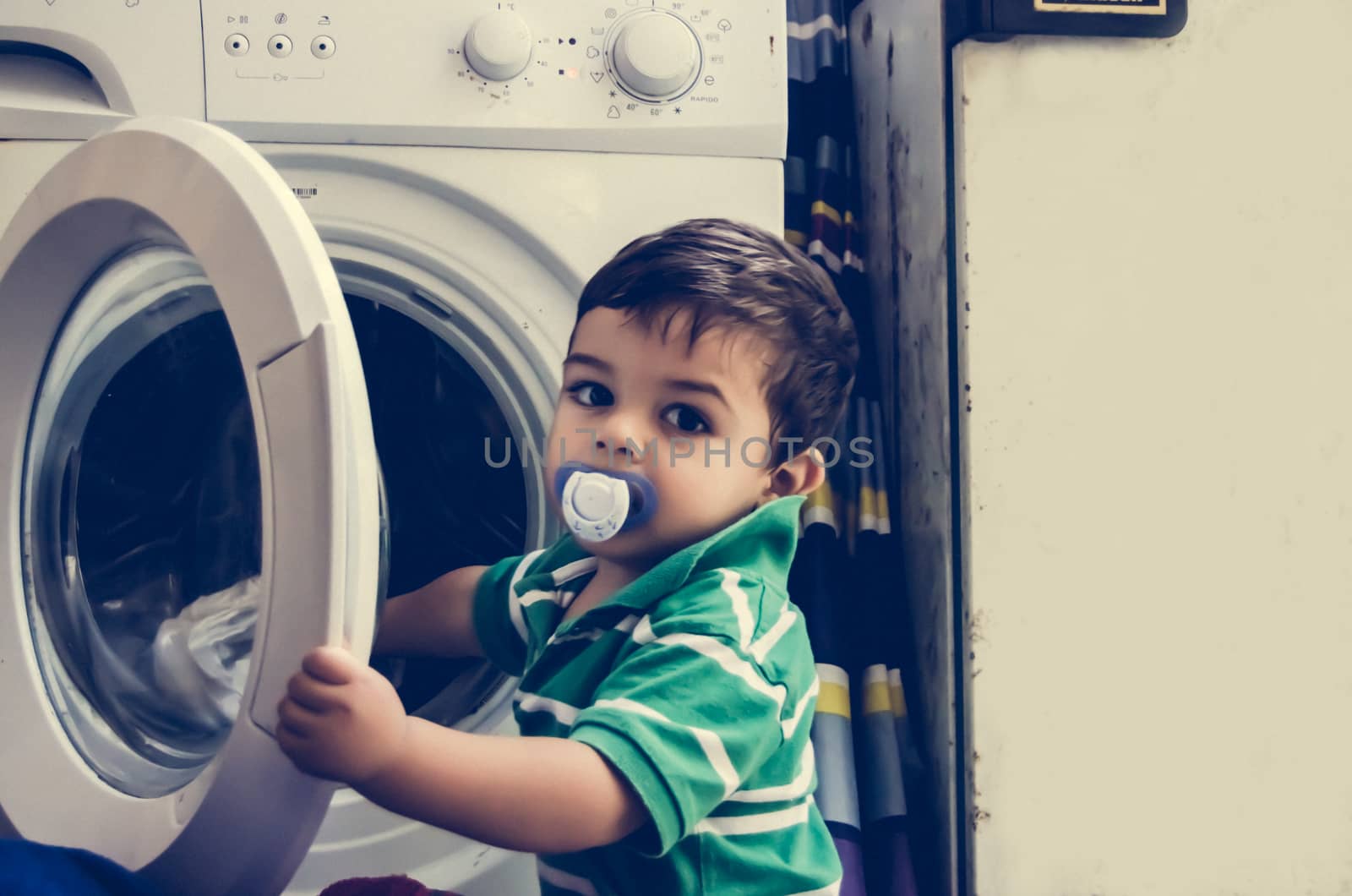 One and the half years old baby boy putting clothes in washing machine by negmardesign