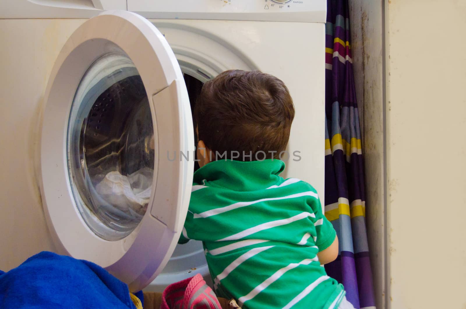 One and the half years old baby boy putting clothes in washing machine by negmardesign