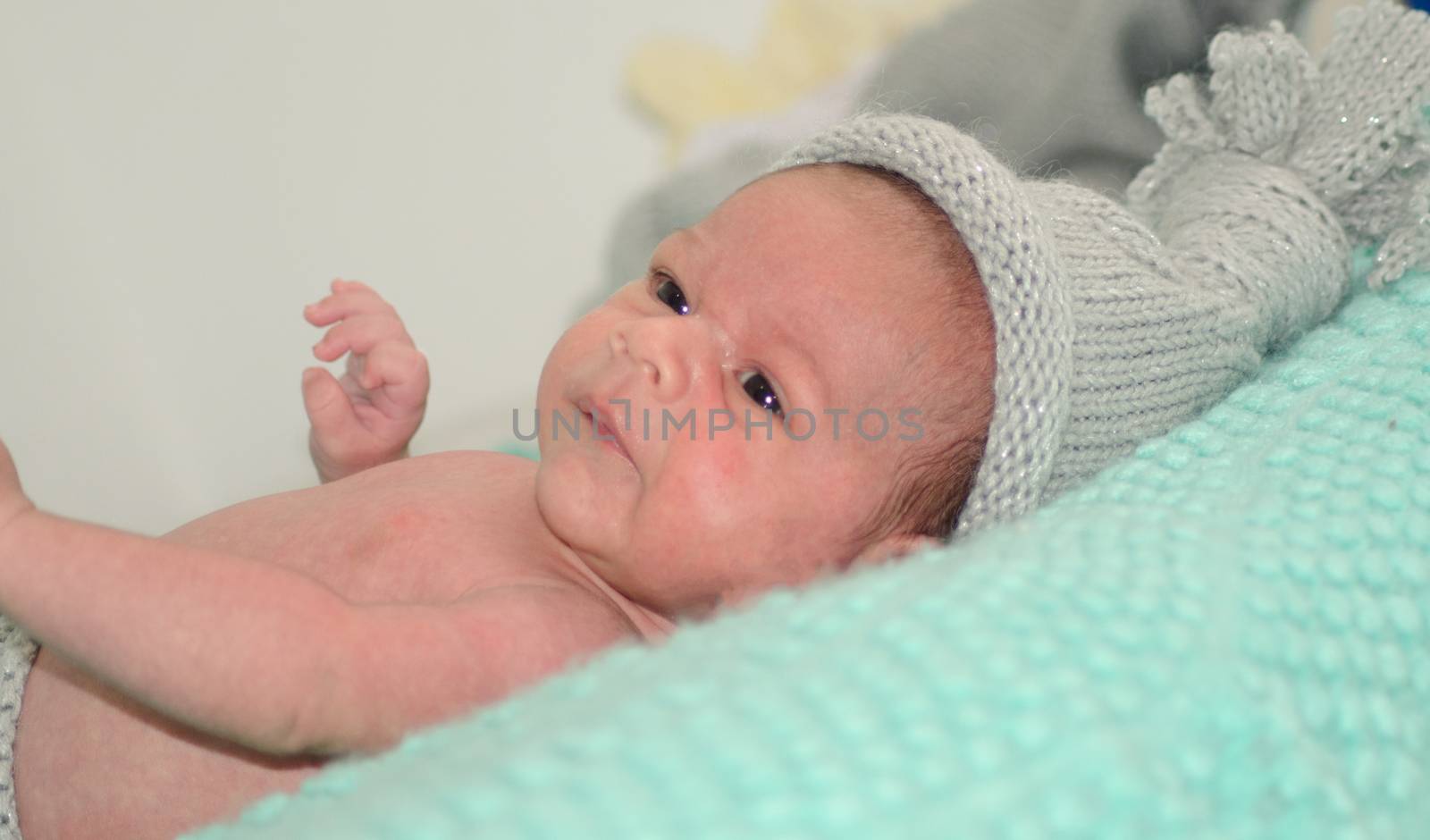 4 weeks old newborn baby boy with gray hat on green blanket