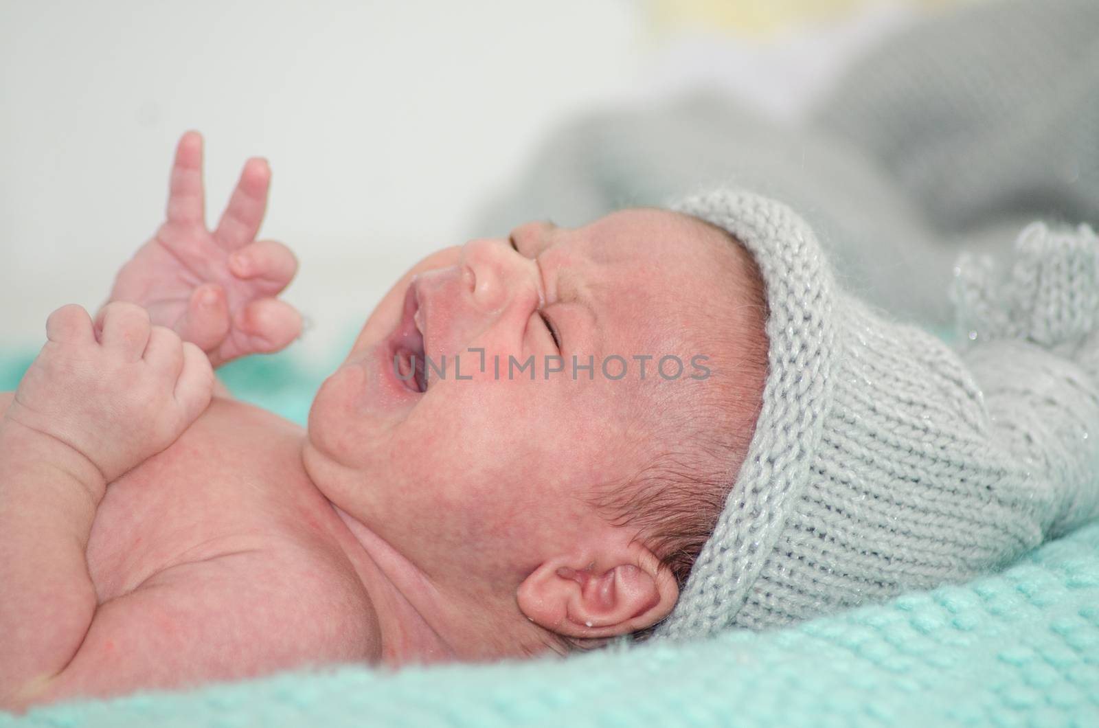 4 weeks old newborn baby boy with gray hat on green blanket crying close up