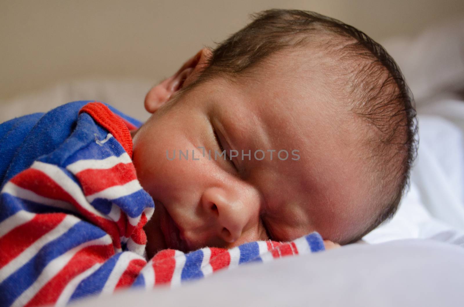 two weeks old newborn baby boy sleeping in blu red pijama on white quilt