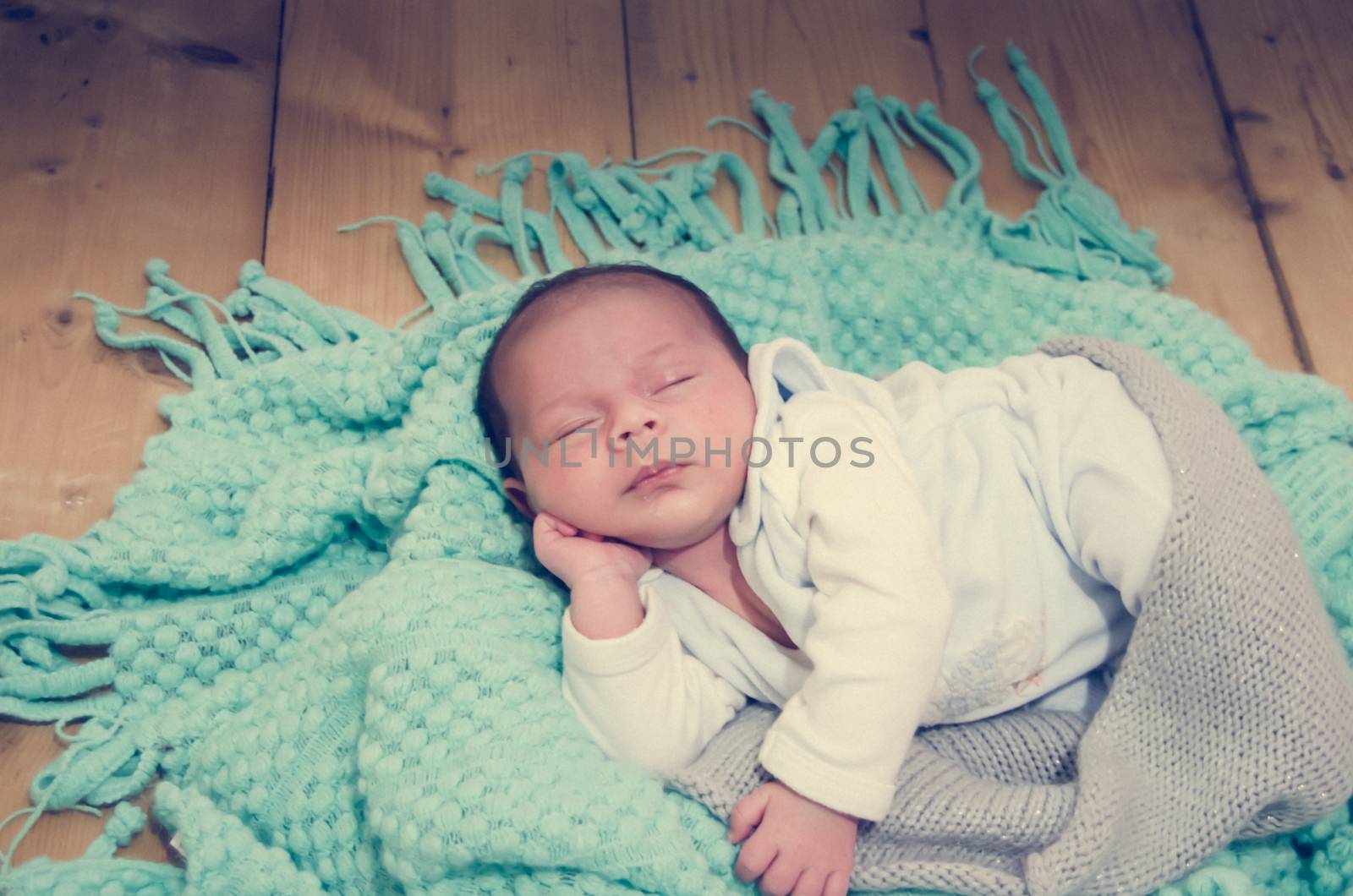 4 weeks old newborn baby boy on green blanket on wooden background by negmardesign