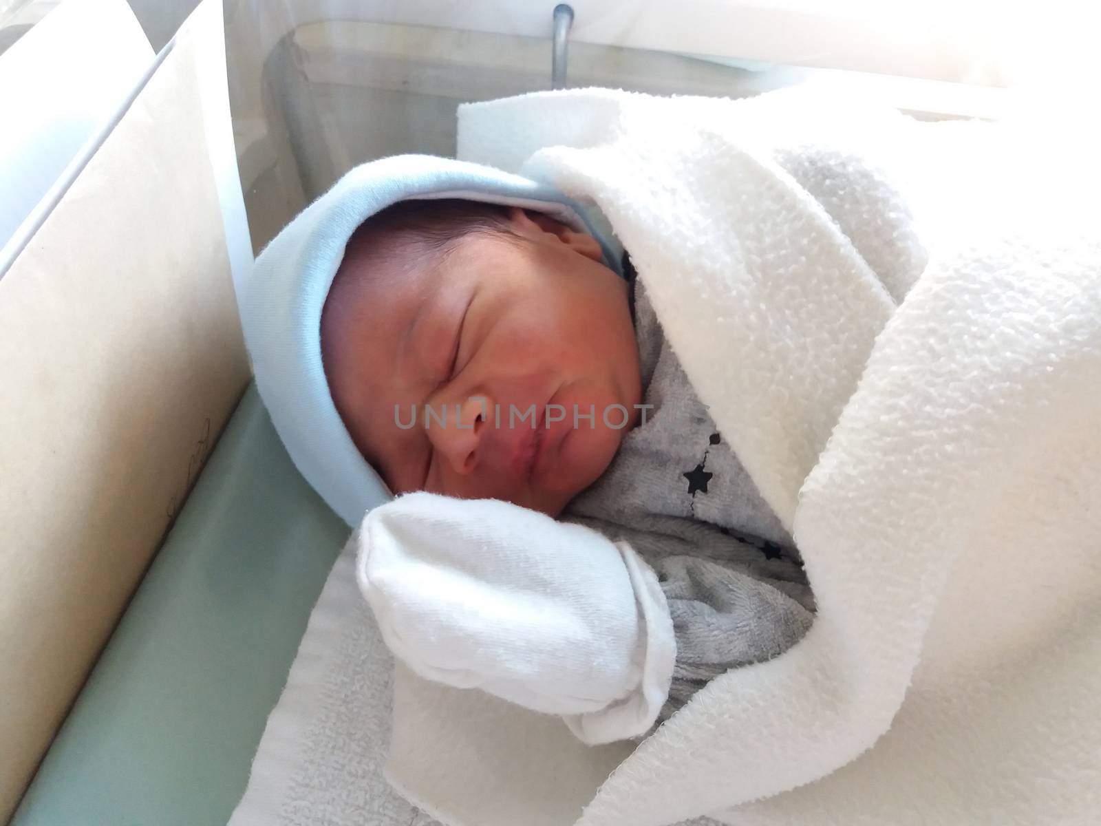 two days old newborn baby boy, sleeping in hospital cot, wraped in white blanket