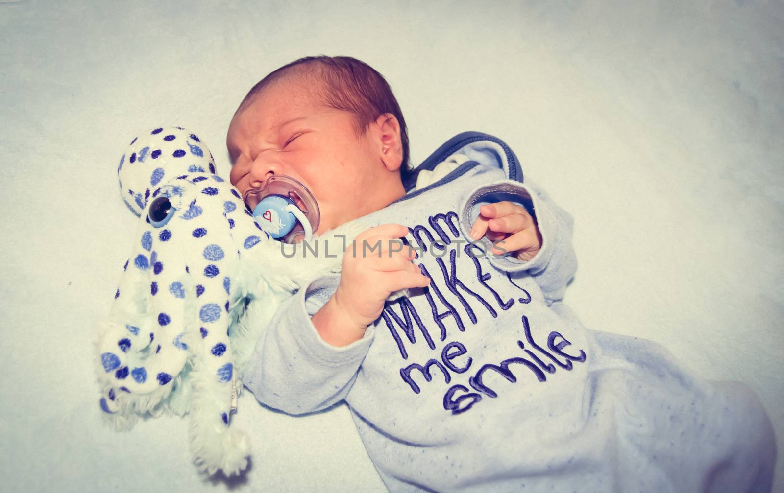 four days old newborn baby boy crying in the cot with octopus soft toy