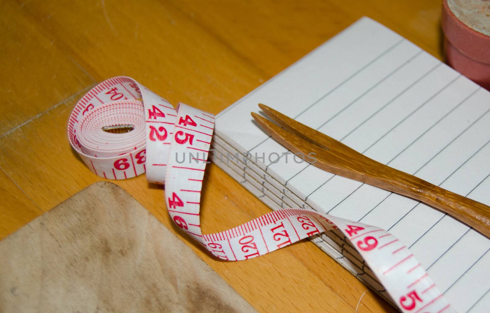 notebook with wooden fork and measuring tape on wooden table, diet and healty eating concept