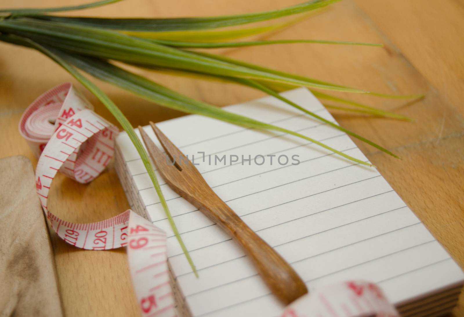 notebook with wooden fork and measuring tape on wooden table, diet and healty eating concept