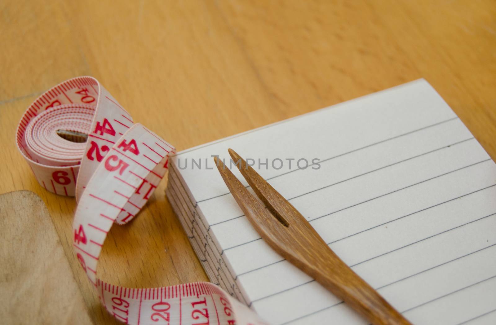 notebook with wooden fork and measuring tape on wooden table, diet and healty eating concept