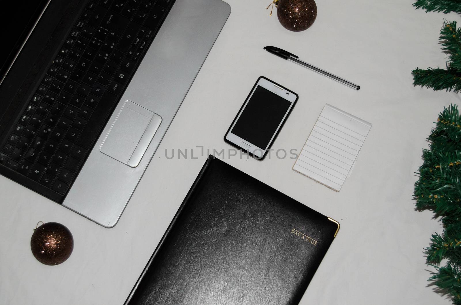 White office desk table with blank notebook, laptop and other office supplies and christmas balls by negmardesign