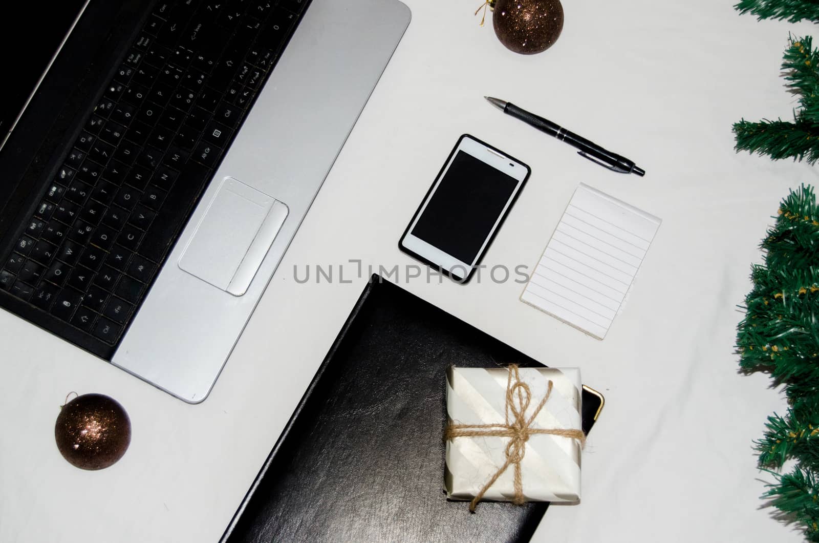 White office desk table with blank notebook, laptop and other office supplies and christmas ornaments with gift box by negmardesign