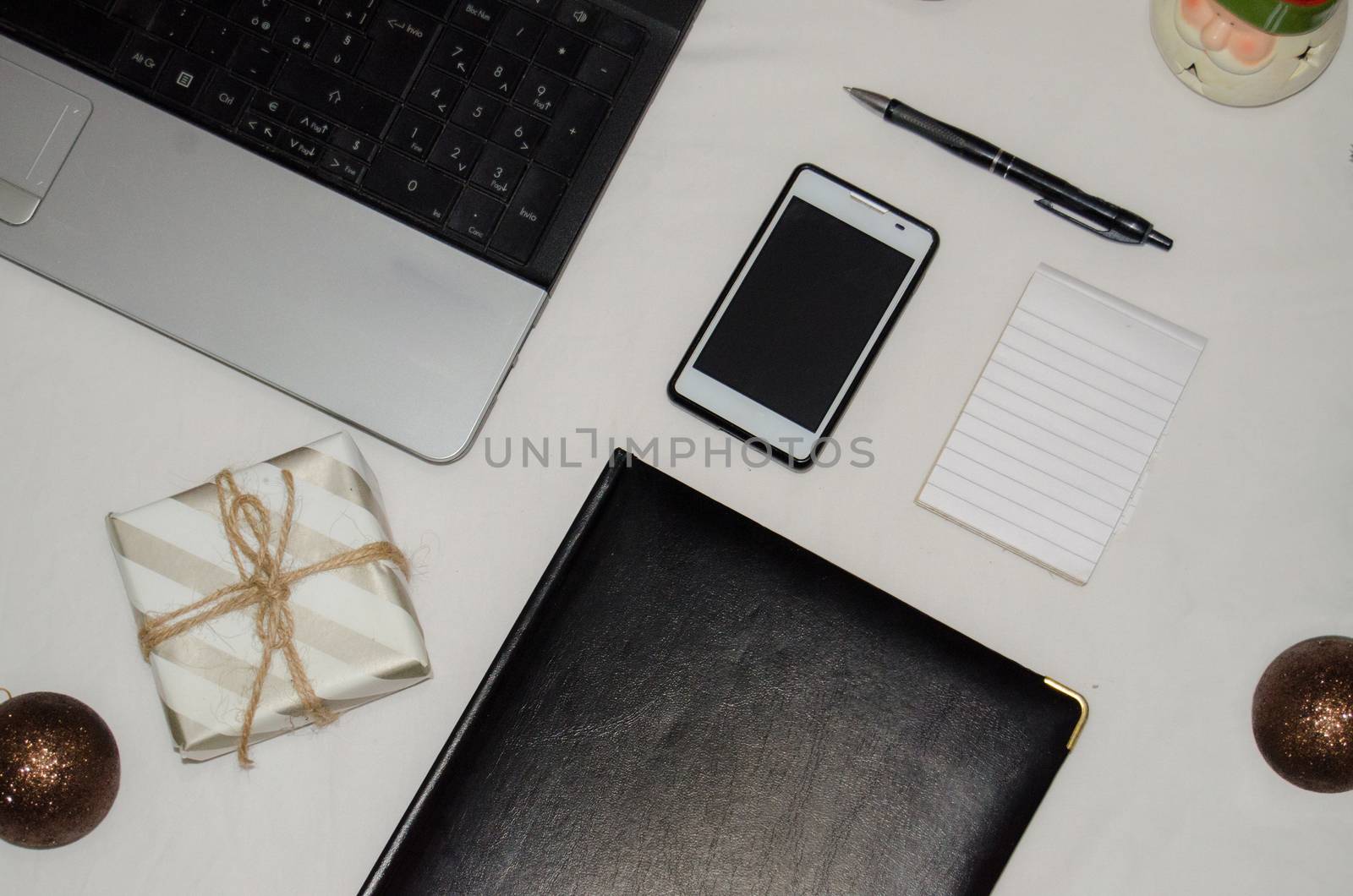 White office desk table with blank notebook, laptop and other office supplies and christmas ornaments with gift box by negmardesign