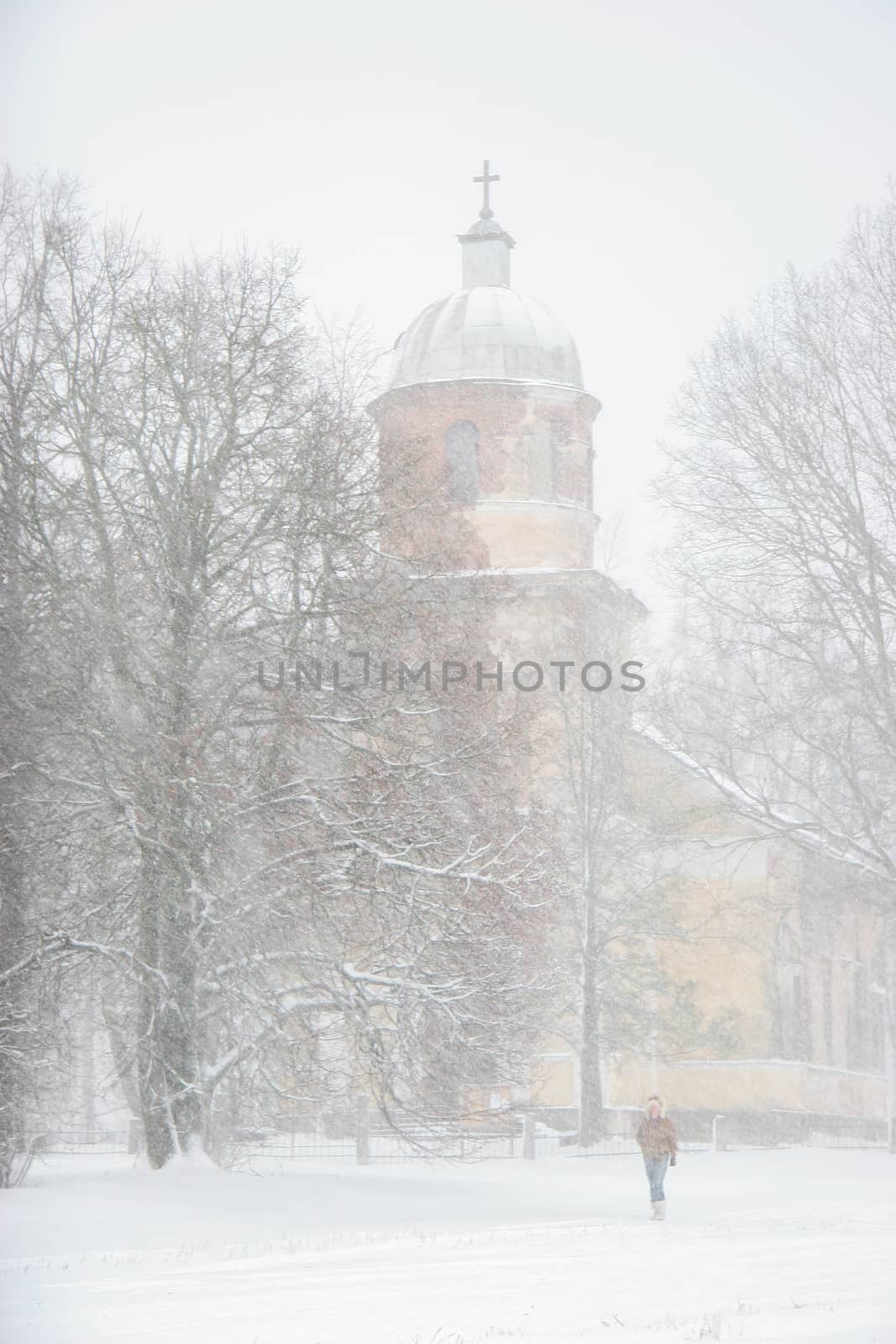 Church in snowfall. Winter in Vecsaule, Latvia. Church covered in snow. Winter scene with snow covered church and trees.



