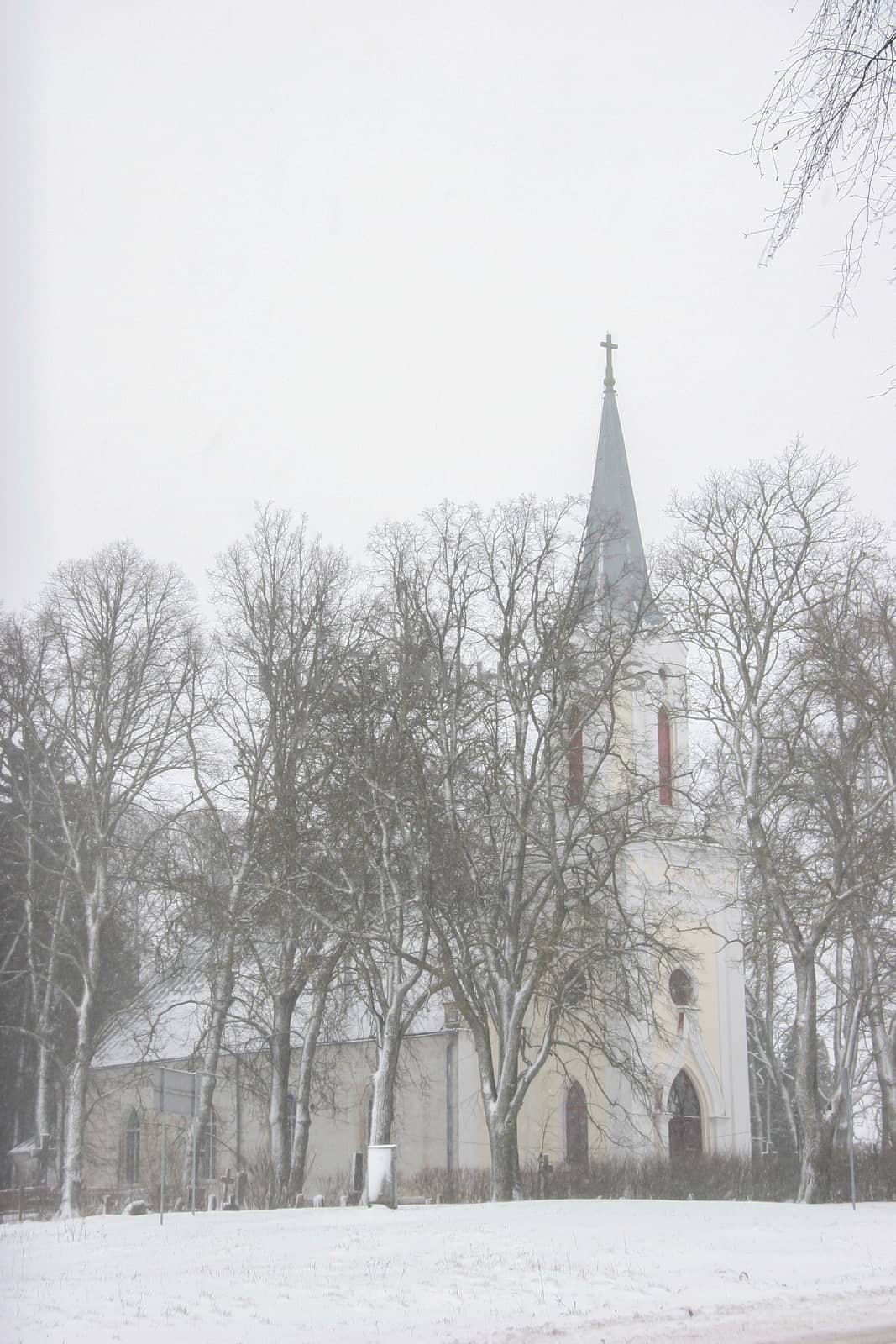 Church in snowfall. Winter in Barbele, Latvia. Church covered in snow. Winter landscape with snow covered church and trees.

