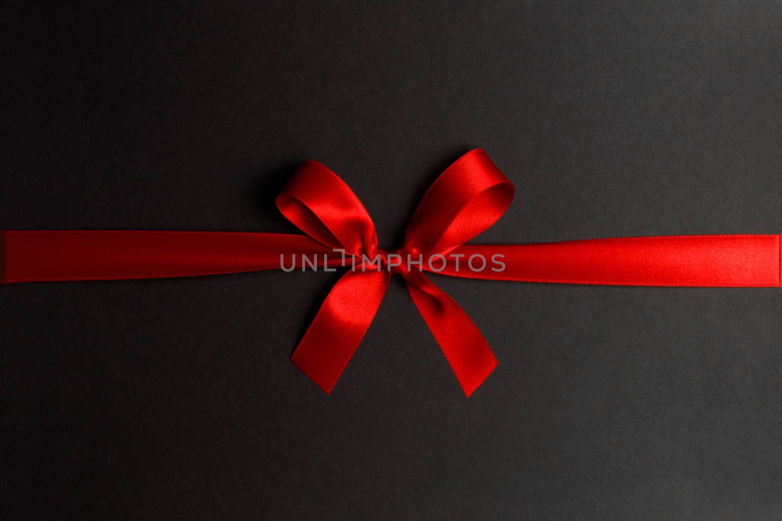 Shiny red satin ribbon and bow on black background. Holiday gift concept