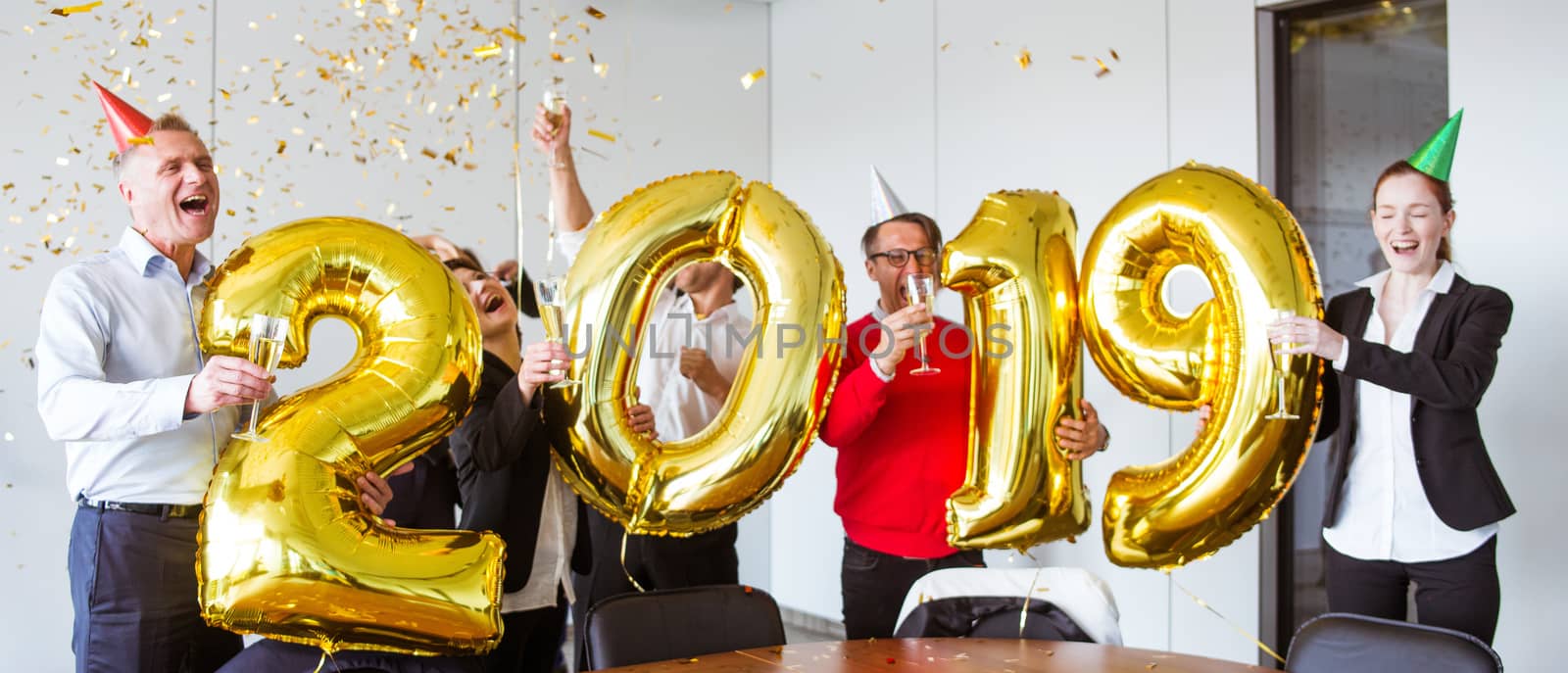 Business people celebrating 2019 New Year at office party holding golden balloons