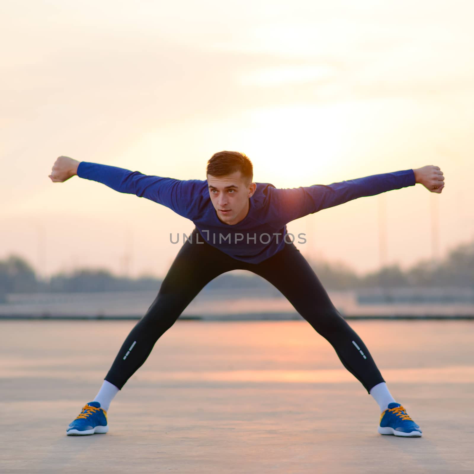 Young Male Runner Stretching Before Run at Sunset. Healthy Lifestyle and Sport Concept. by maxpro