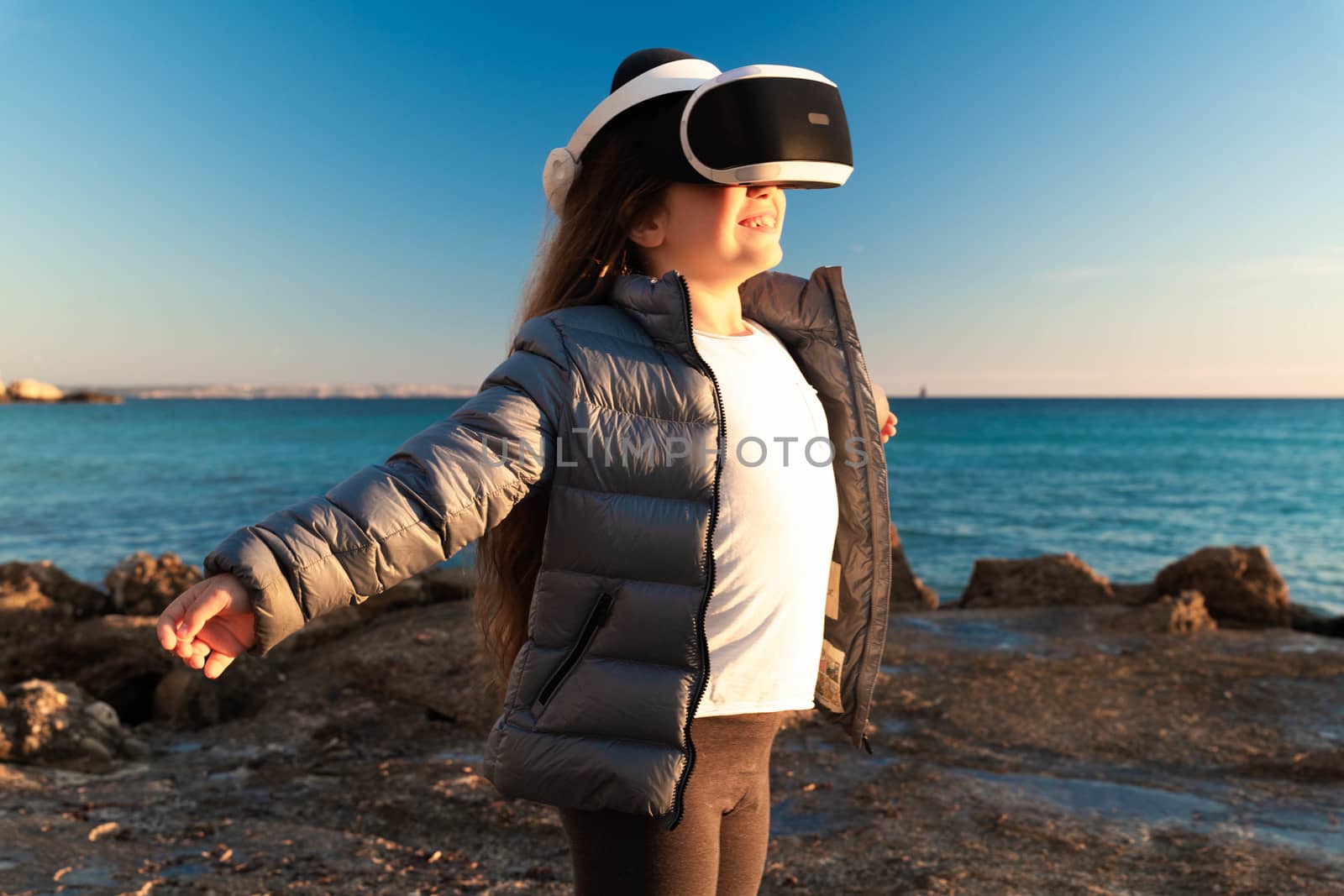Happy girl with open arms, wearing virtual reality headset 3d on the beach.