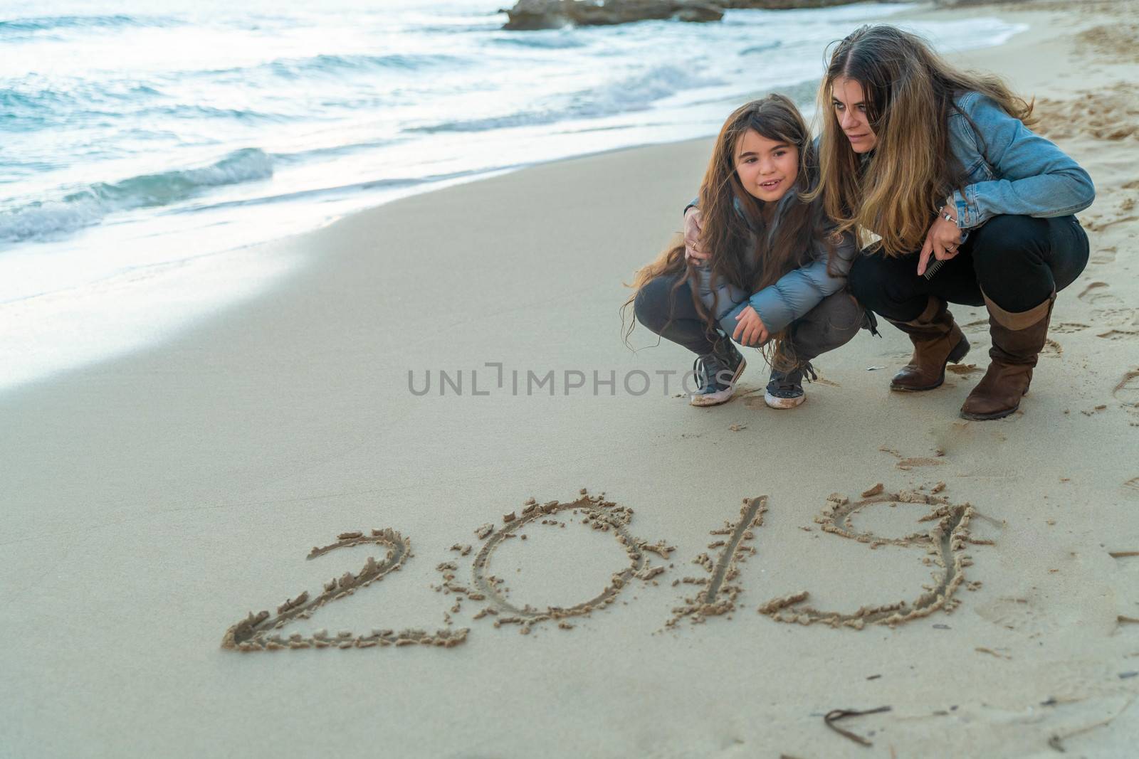 Mother and daughter looking at 2019 written on the sand by Lordignolo