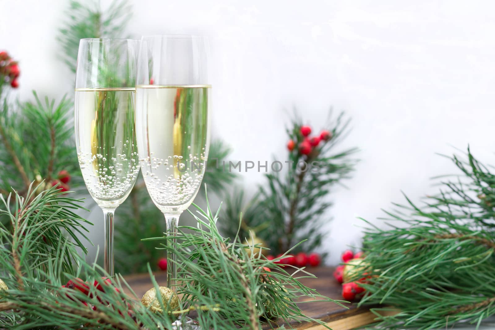 Christmas and New Year seasonal composition with pine tree branches, two glasses of champaign, golden balls ornament and red rowan berries