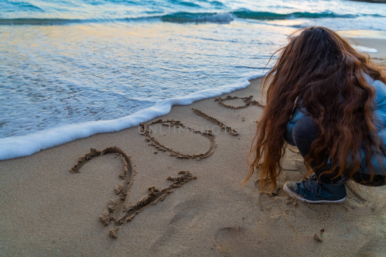 Girl with long hair writing 2019 on the beach with the wave coming close to the writing