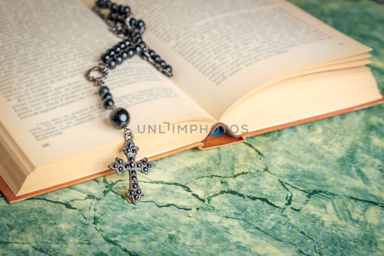 Black rosary and cross on the Bible on a green surface. Religion at school.