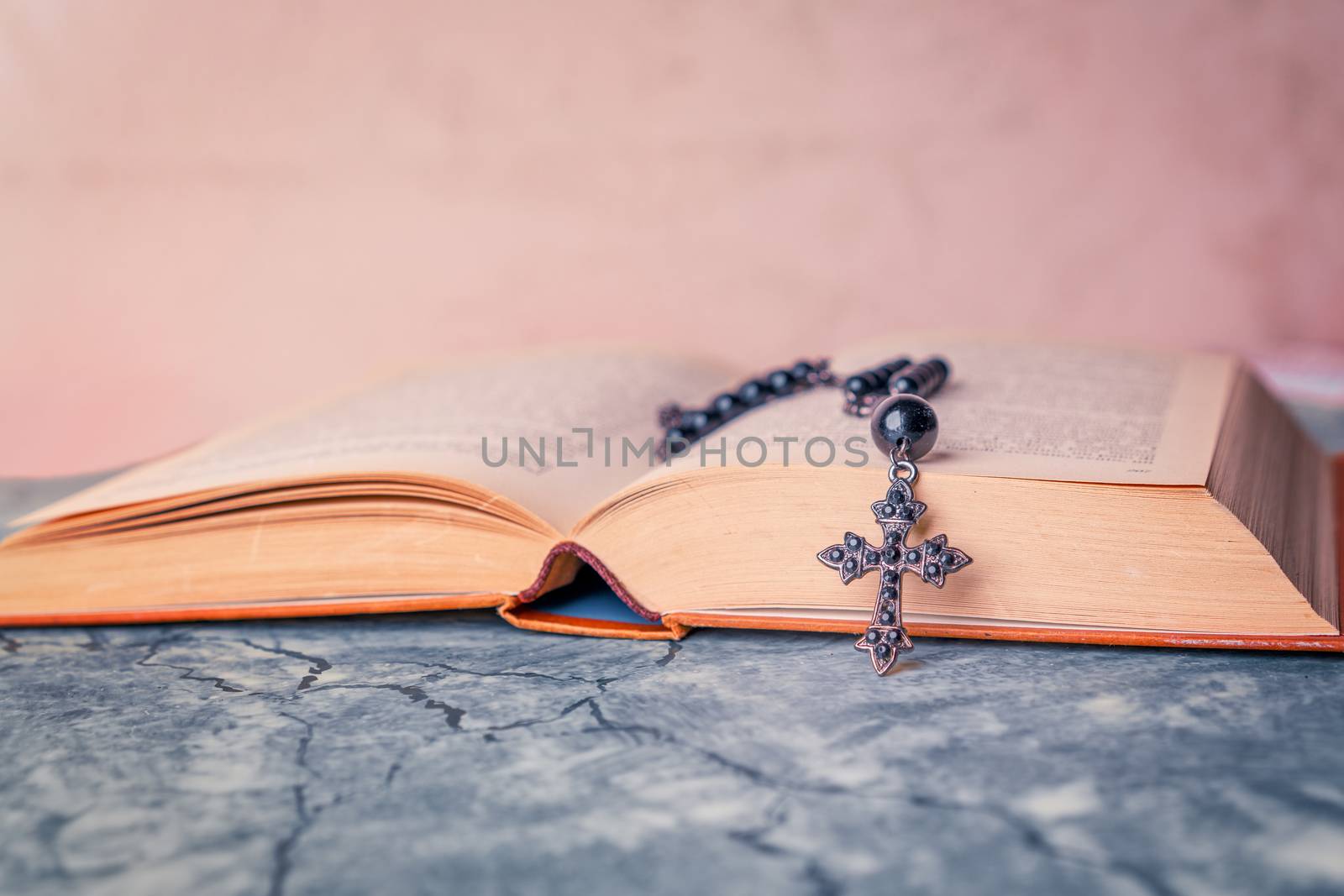 Black rosary and cross on the Bible on a gray table. Religion at school.