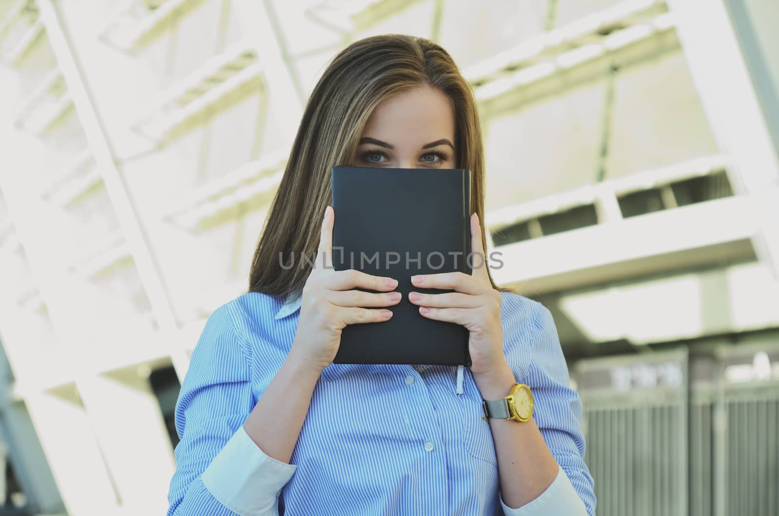 A young girl in office clothes holds a notebook with her hands, covering half of her face