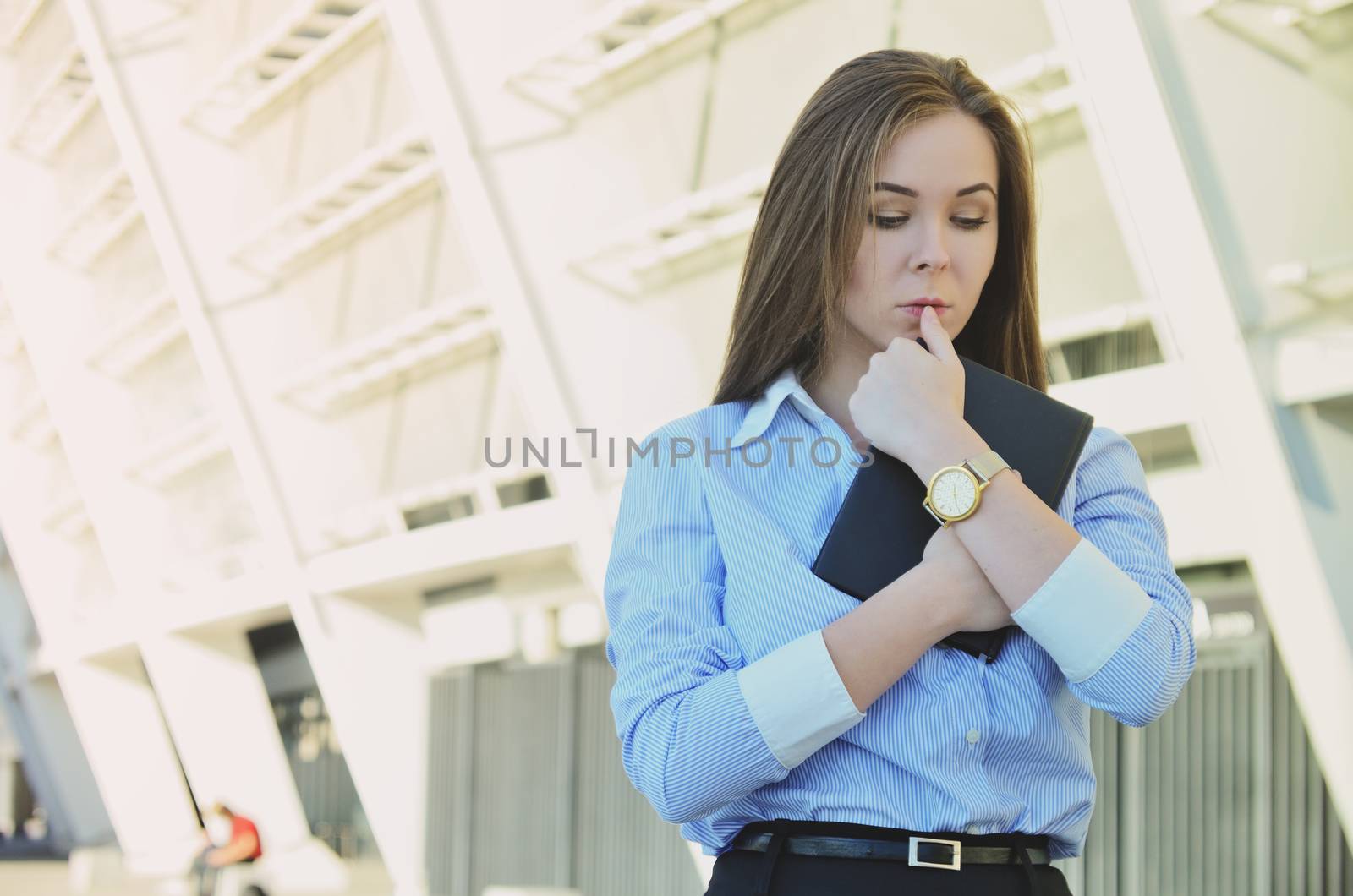 Young beautiful business lady in office clothes holding a notebook in her hands, thinking about the problems