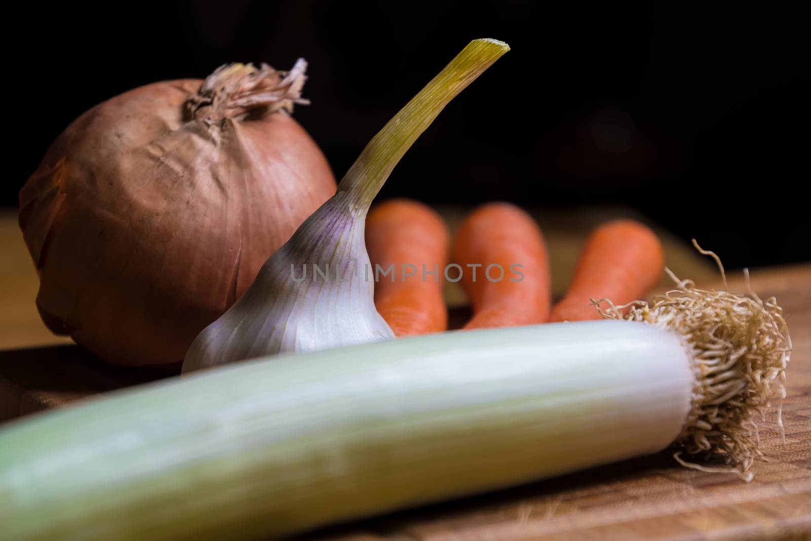 onion, leek, garlic and carrots on a table in the kitchen with dark background