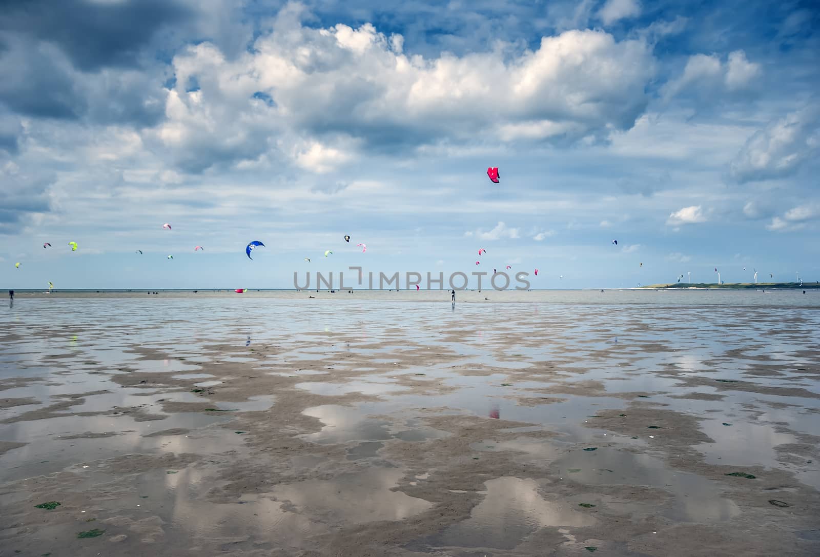 people sporting and kite surfing on the beach with clouds in the sky on a beach in holland