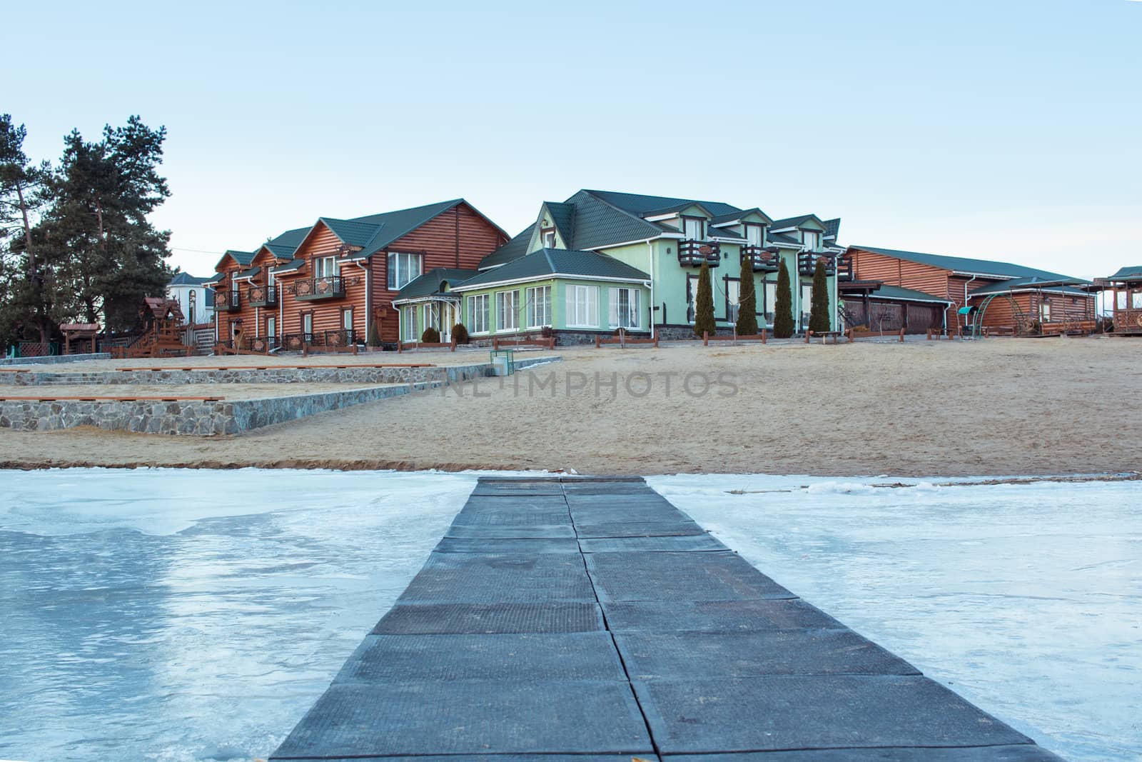 Winter village house on sandy beach near cold frozen river lake