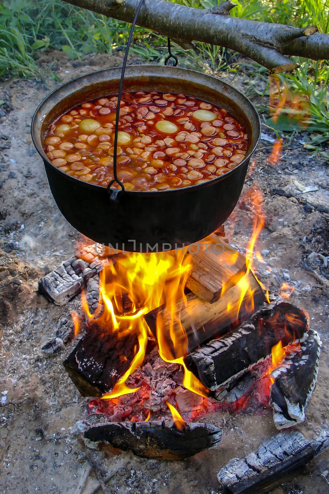 Cooking soup in cast iron boiler on burning campfire. Pot with soup over the open fire outdoors. Tourism in Latvia. Soup cooking on the fire outdoor for camping trip.