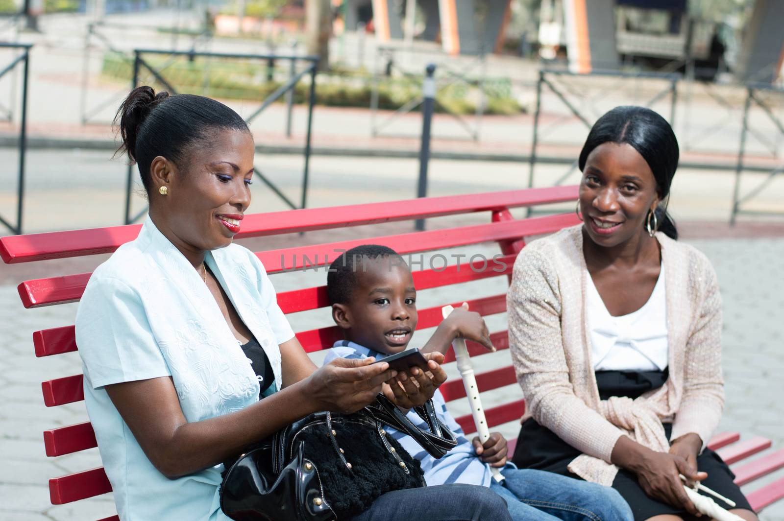 two young women sitting on a bench are talking with a little boy in the middle.