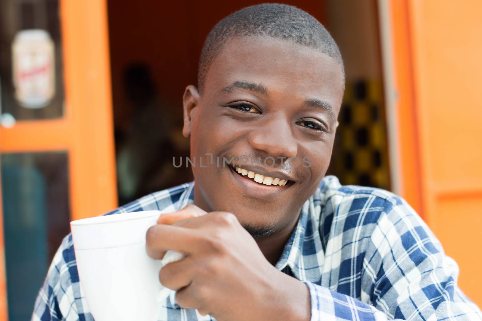 This happy young man holding a cup of coffee in hand.