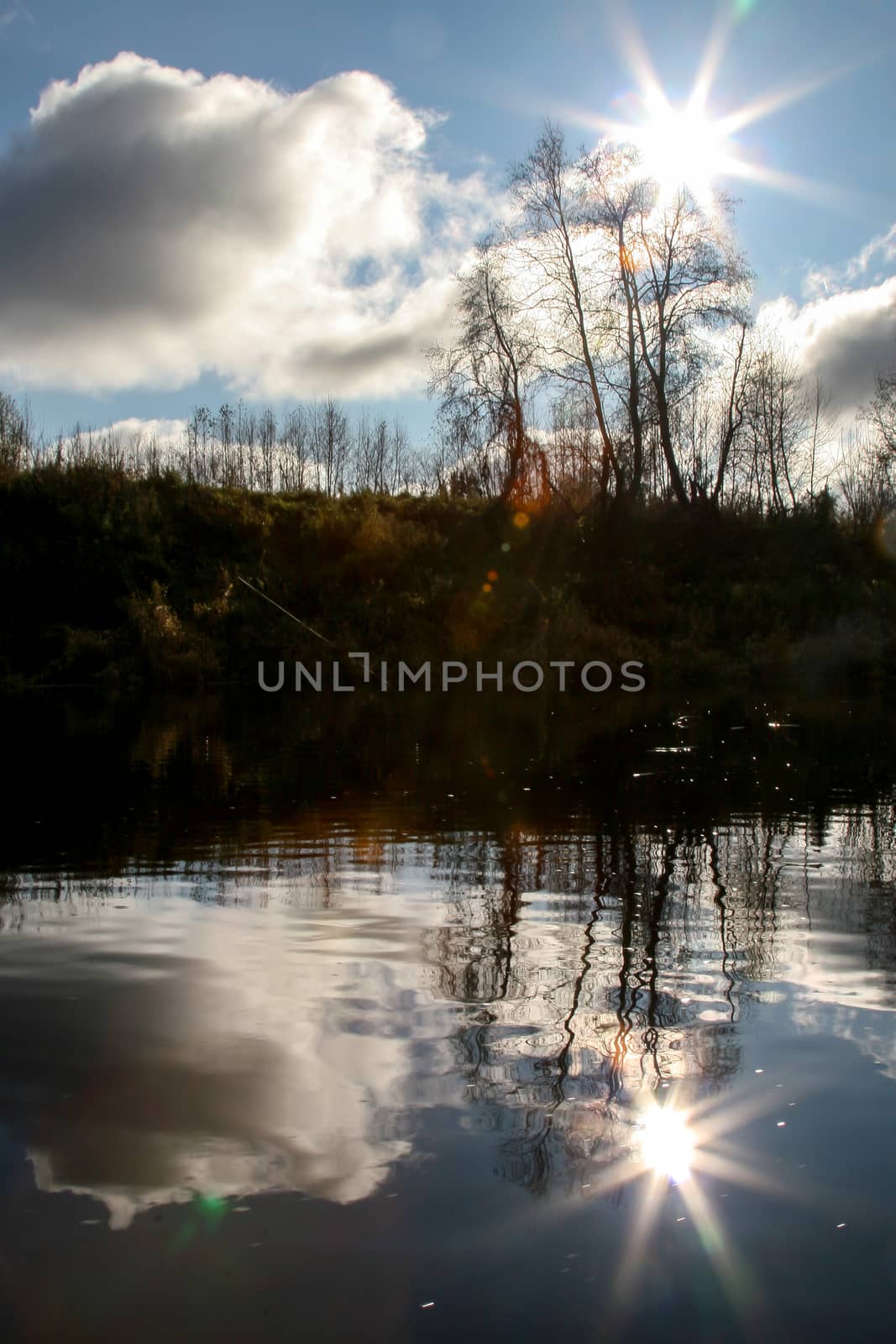 View on autumn landscape of river and trees in evening. Forest on river coast in autumn evening. Reflection of autumn trees, clouds and sun in water. Autumn in Latvia. Autumn landscape with colorful trees and river. Evening reflection in river.