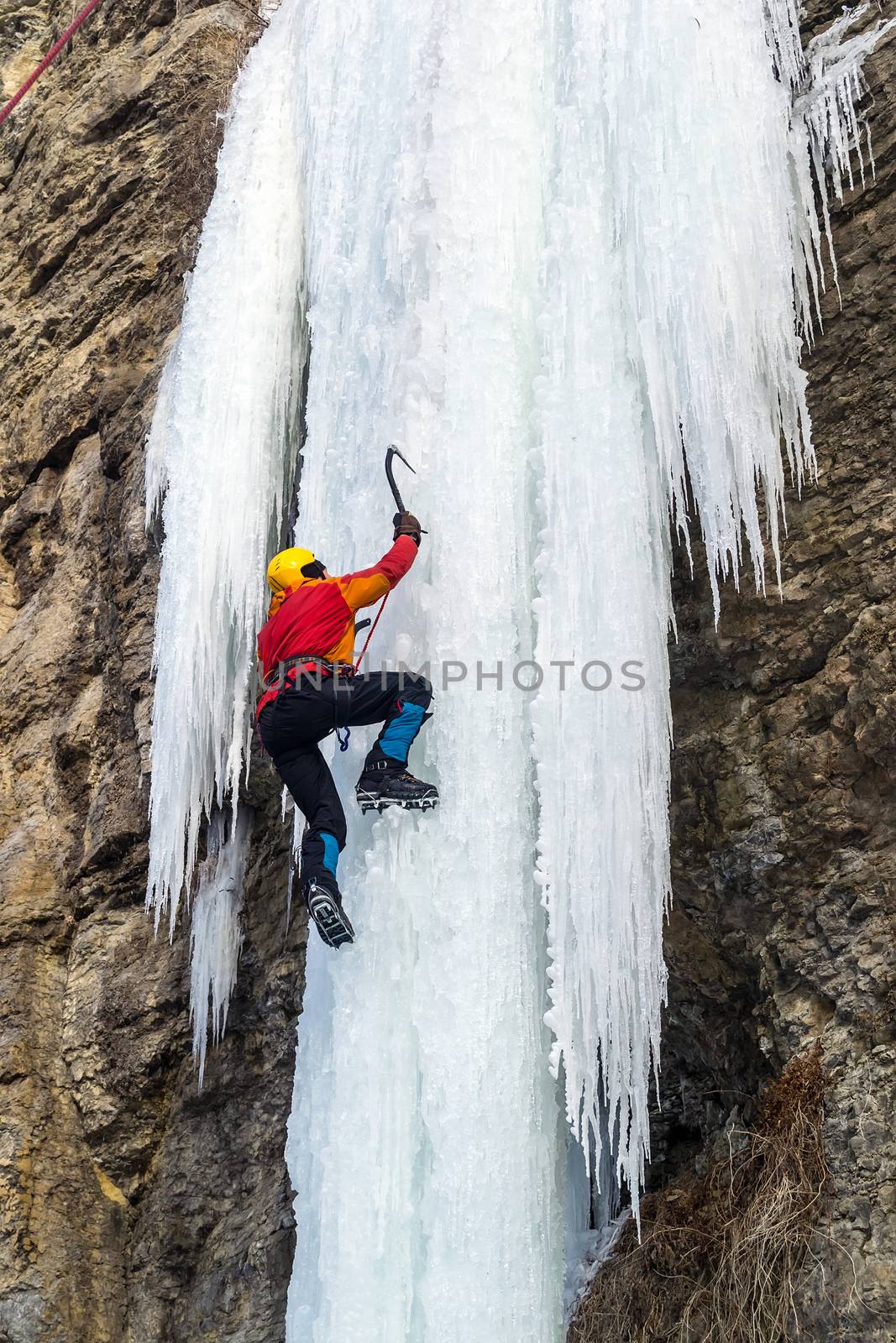 Extreme ice climbing. Man climbing the frozen waterfall using ice axes and crampons.