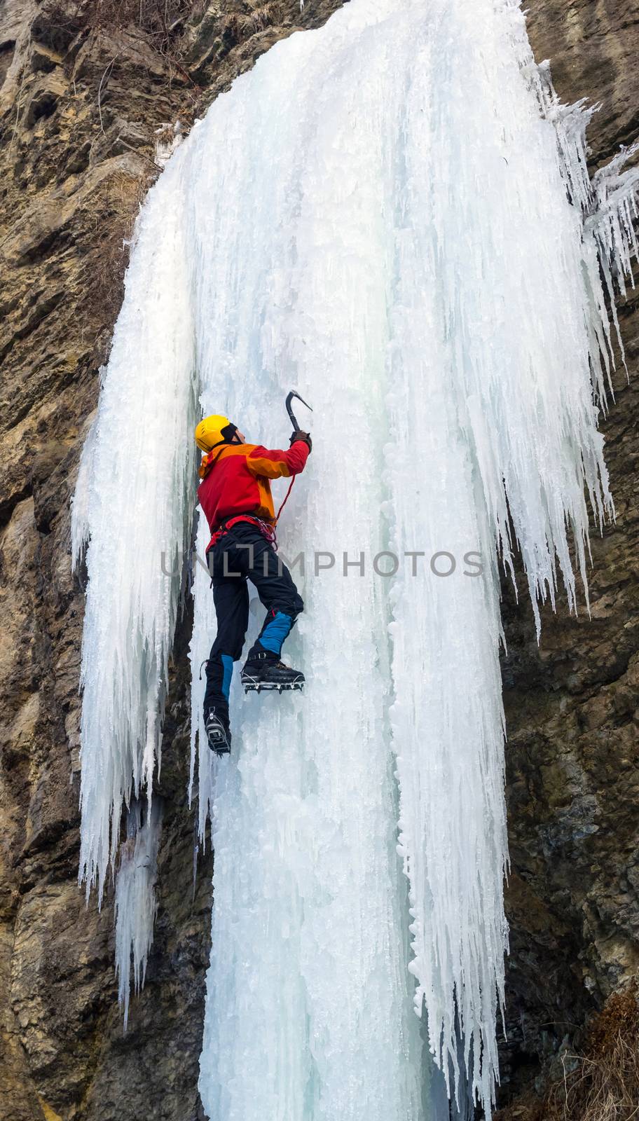 Man climbing the frozen waterfall using ice axes and crampons. Extreme ice climbing. Winter
