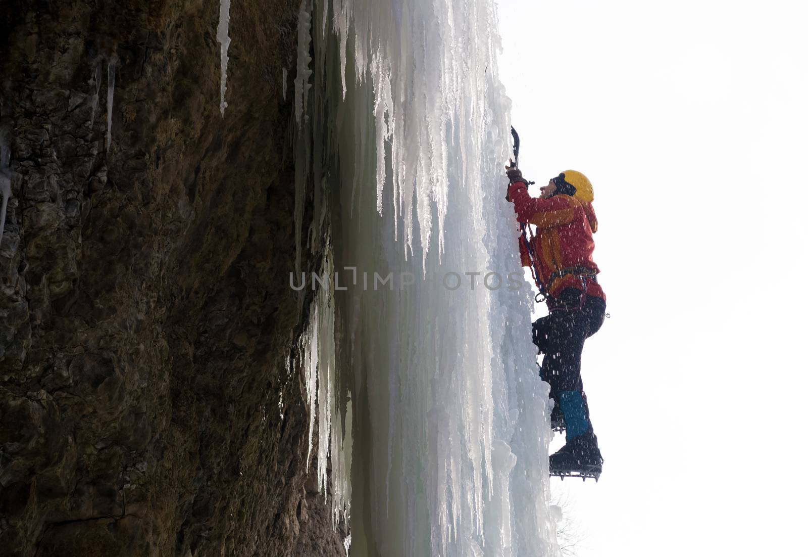 Extreme ice climbing. Man climbing the frozen waterfall using ice axes and crampons. Winter