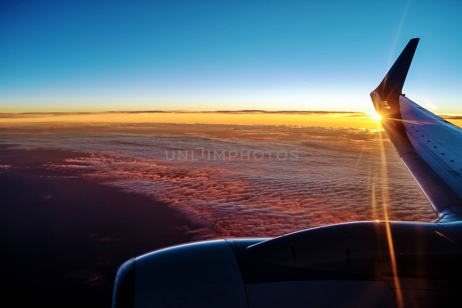 Sunset from a plain. View through the window of an aircraft. Wing of the plane above clouds.