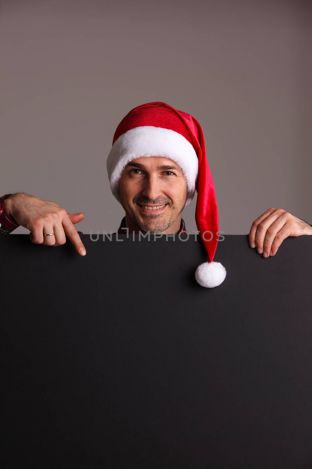 Man wearing santa christmas hat holding and pointing blank billboard or placard sign copy space for text advertising