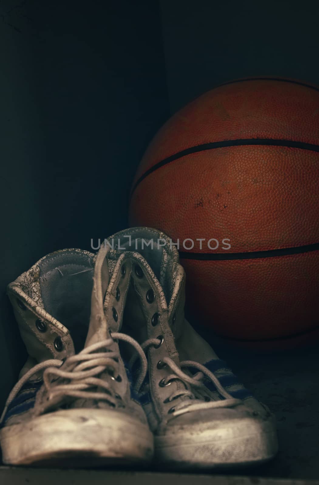 Close up pair of old worn sport sneakers shoes and one basketball ball in locker, low angle view