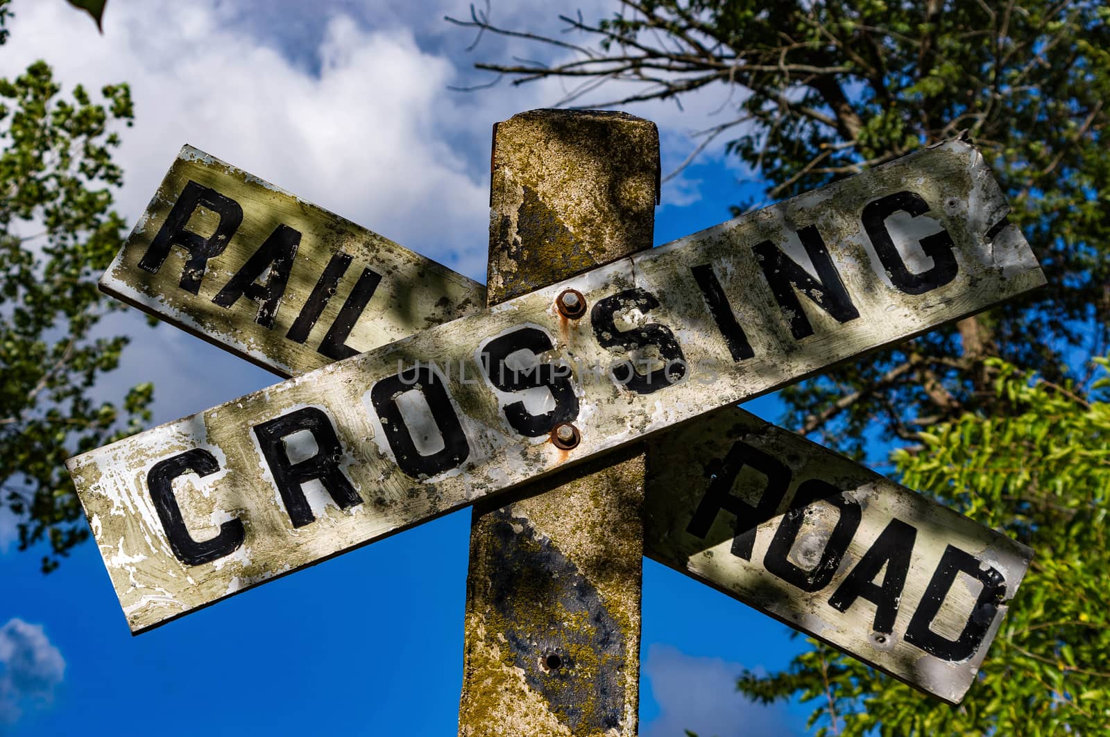 Railroad crossing sign with blue sky background with clouds.