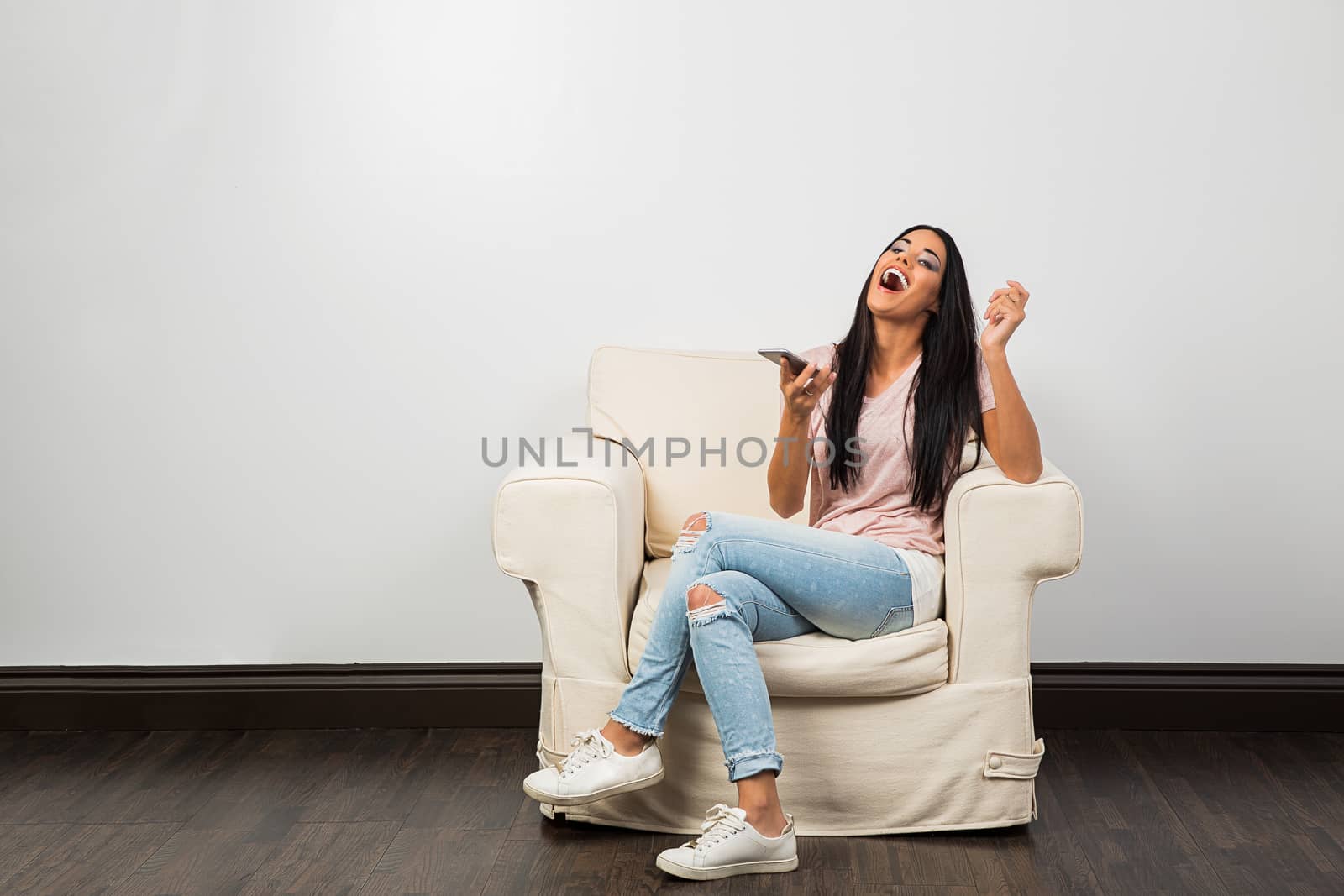 young woman, sitting on a couch, laughing out loud, with a smart phone
