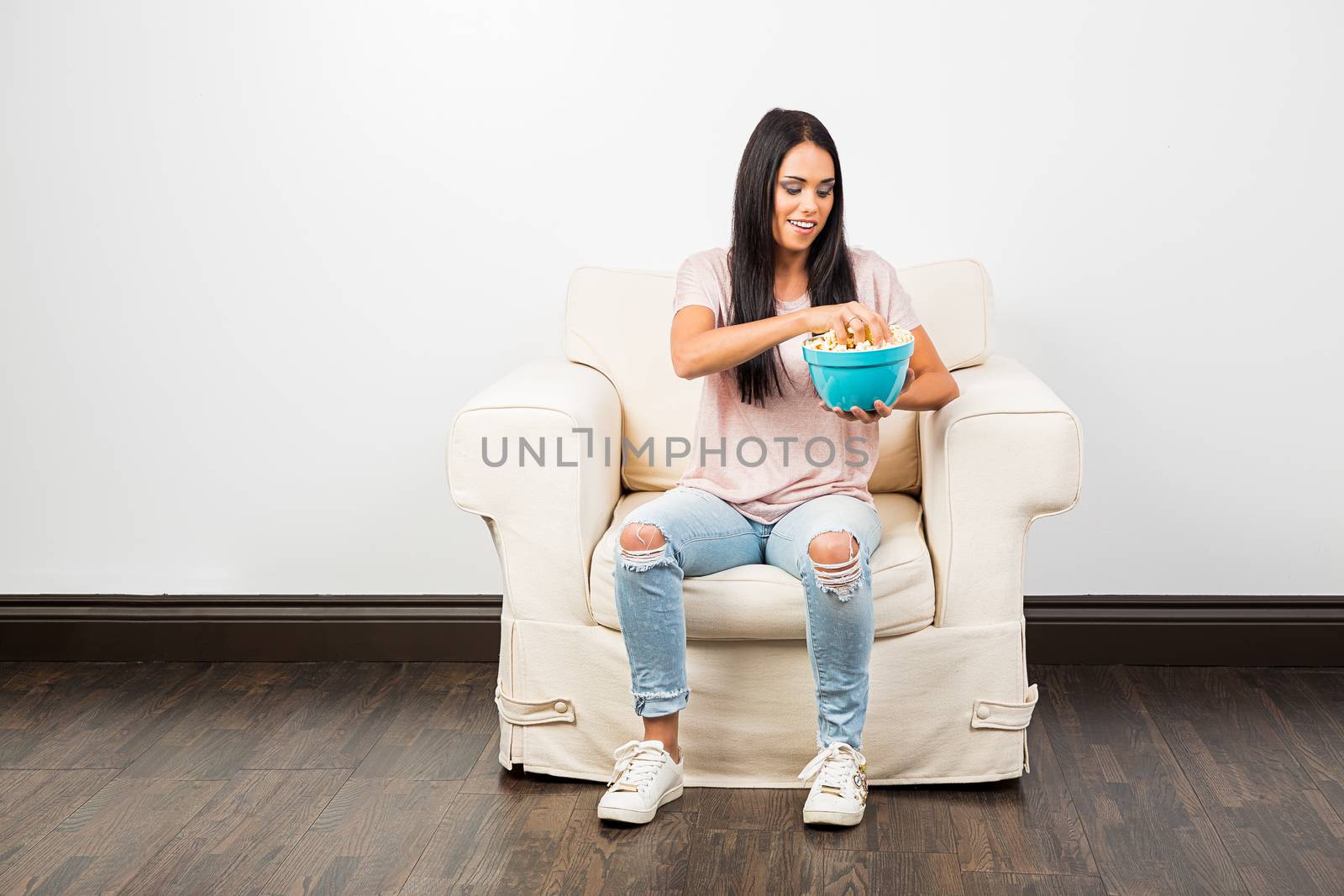 young woman in her twentie, sitting on a couch and eating popcorn