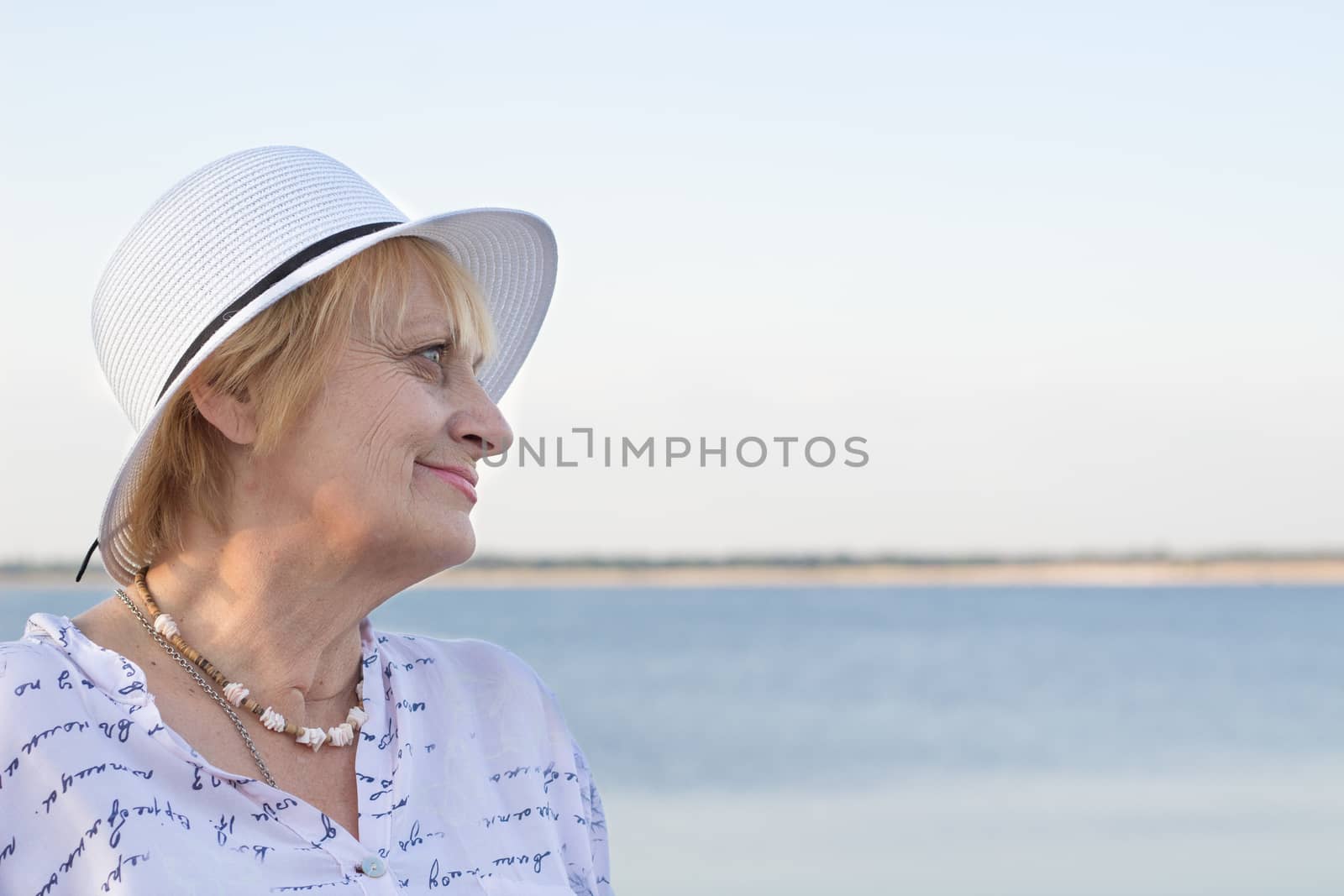 Happy smiling elederly retired lady woman rests in nature near lake river sea