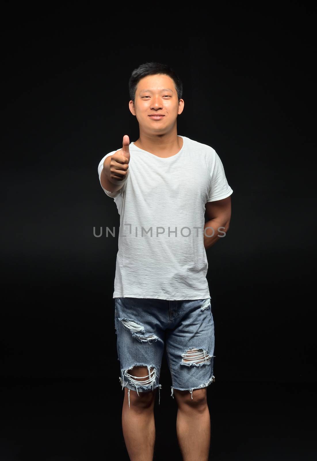 Portrait of a male Asian student of appearance on a black background that shows a thumbs up