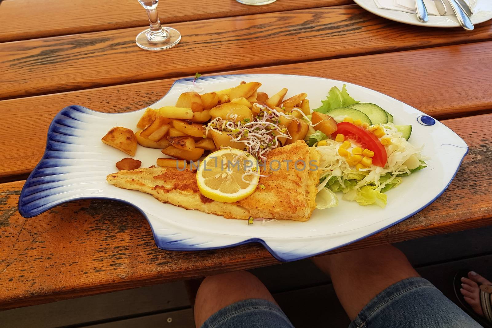 Fried fish with fried potatoes and lemon slices on fish-shaped plate