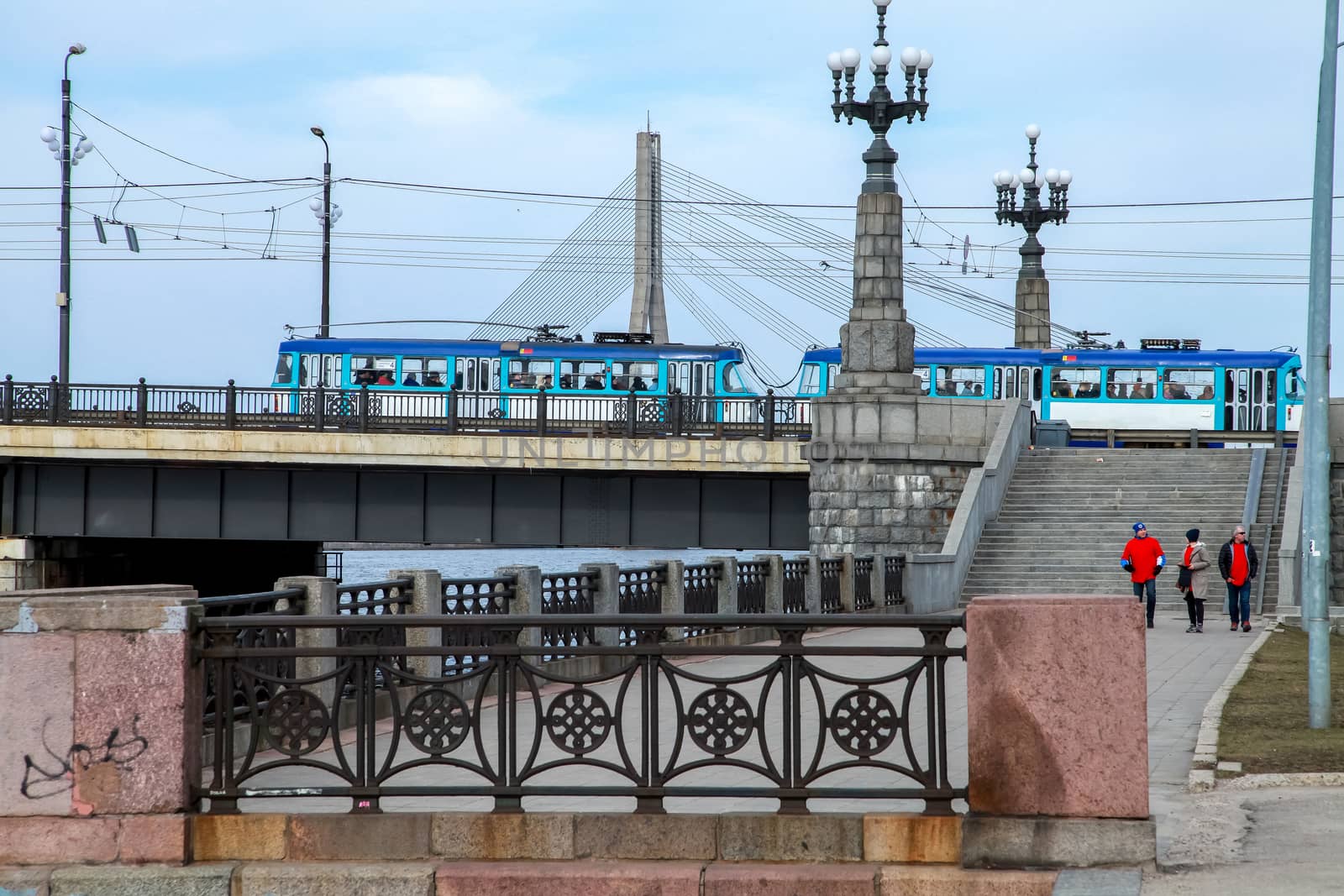 View of the Akmens bridge from the 11th November Embankment. Stairs to the stone bridge and lanterns in Riga, Latvia. Behind the Akmens bridge-  Vansu bridge. Two bridges on the blue sky background in Latvia. Bridge crossing tram and pedestrians. 