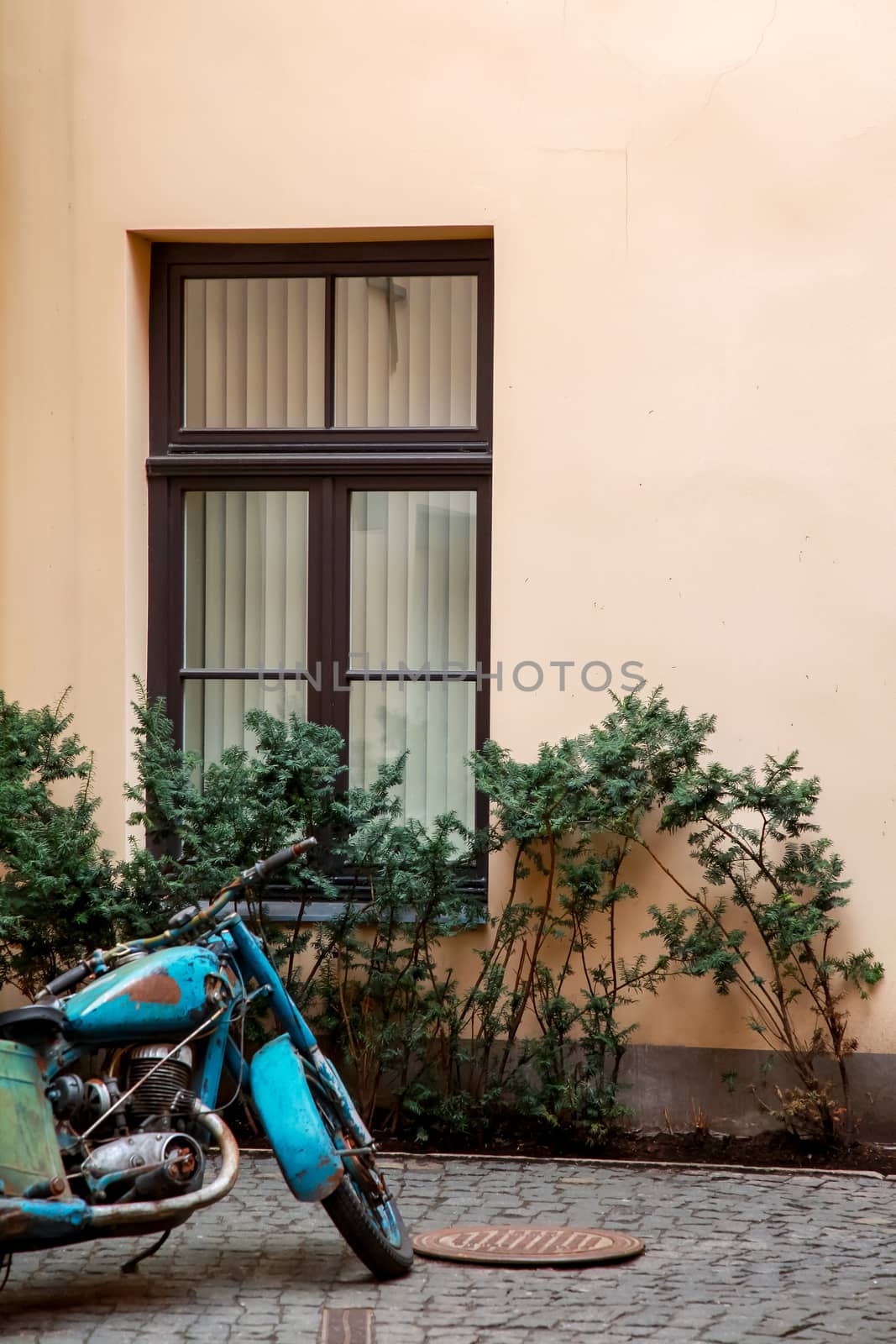 Fragment of beige wall with window in Old Riga, Latvia. Ancient motorcycle next to the wall.