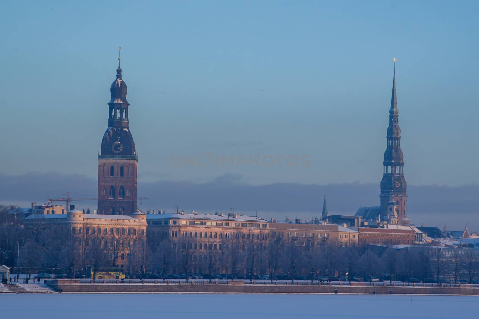 Riga view in winter. Riga, capital city of Latvia in winter time. View of St Peter's Church and St. Jacob's Cathedral. View of Old Riga with frozen river Daugava in the foreground. City Riga with background of blue sky. 